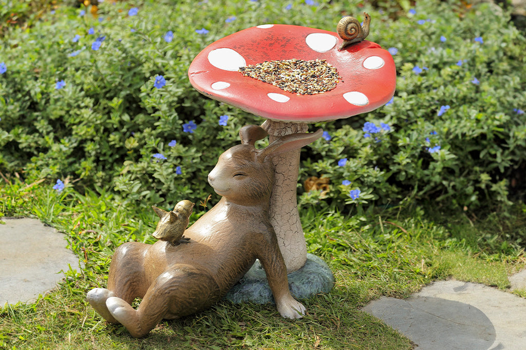 Bunny under a toadstool sculpture with chick and snail - mushroom is birdbath/birdfeeder, shown in garden