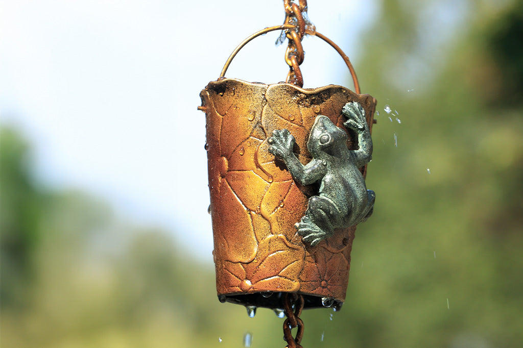 Closeup outdoor view of rain cup on a rain chain. Shown with water cascading over the frog and lilypad motif