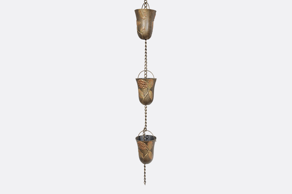 A close up of 3 cups of a rain chain with 8 cups decorated with pine cone motifs.
