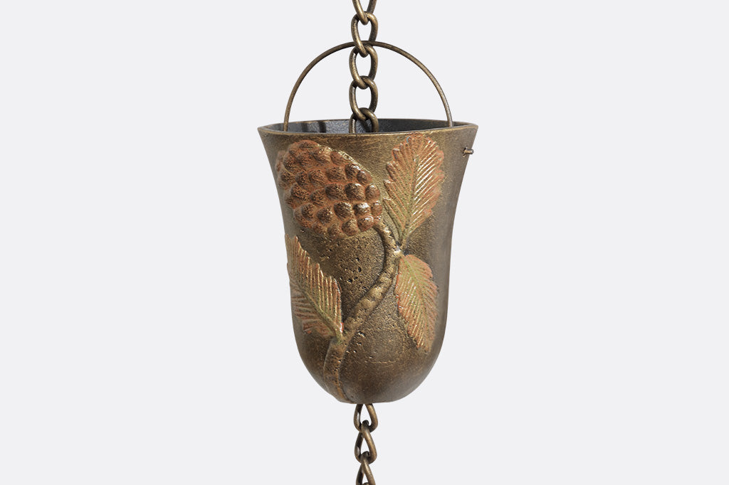 A close up of one cup of a rain chain with 8 cups decorated with pine cone motifs.