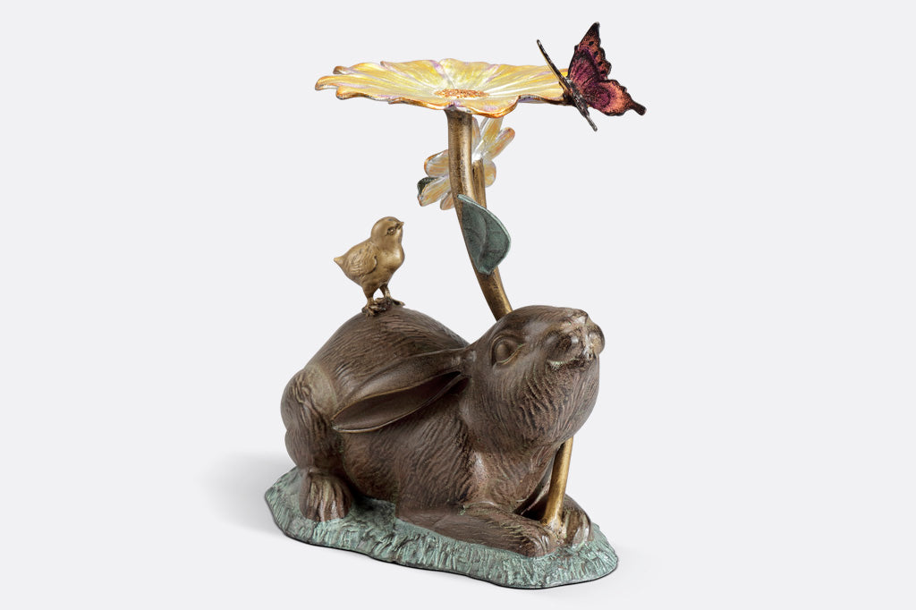 rabbit sculpture and birdbath/birdfeeder. A rabbit holds a blossom, surrounded by a chick, butterfly, and caterpillar