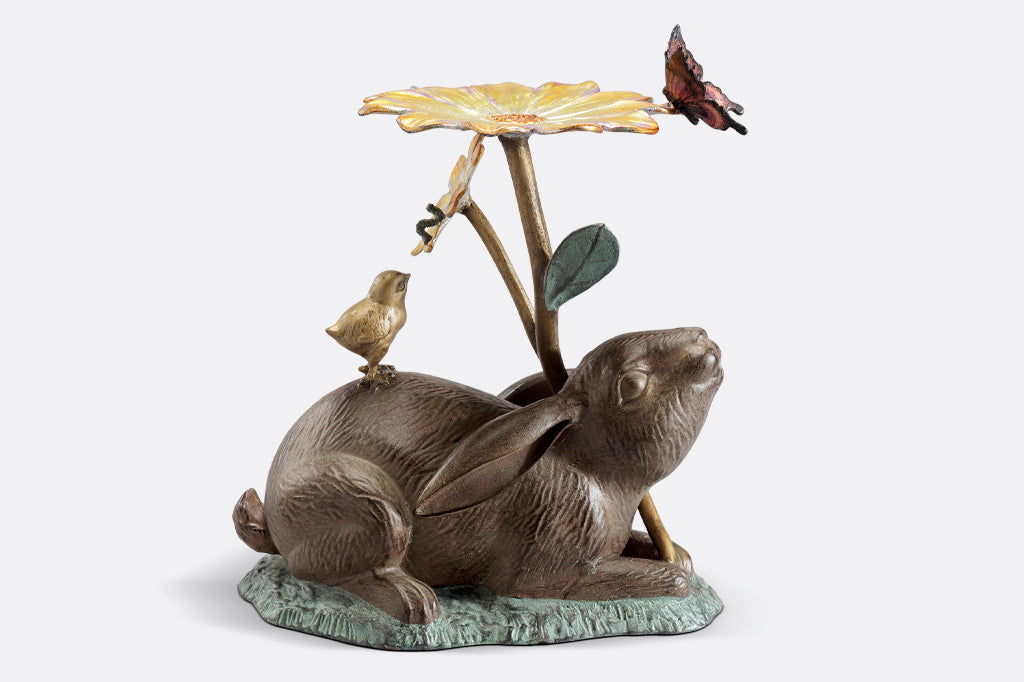 rabbit sculpture and birdbath/birdfeeder. A rabbit holds a blossom, surrounded by a chick, butterfly, and caterpillar