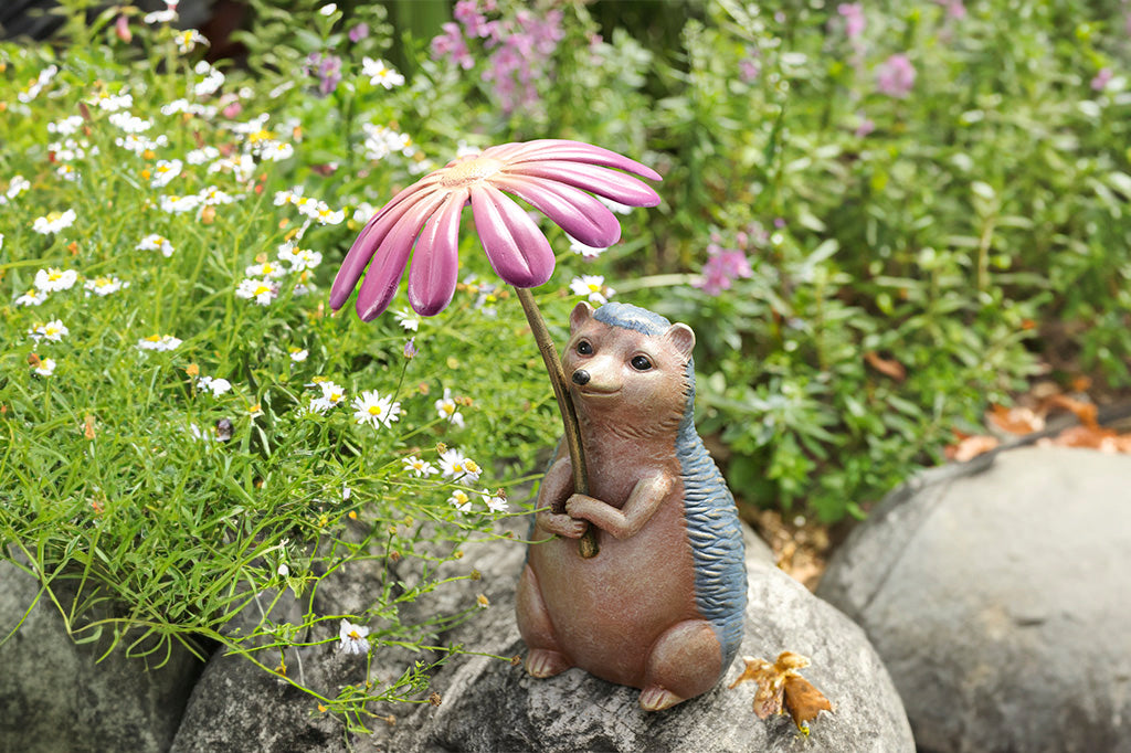 Garden sculpture of hedgehog holding flower blossom like an umbrella - shown in flower garden