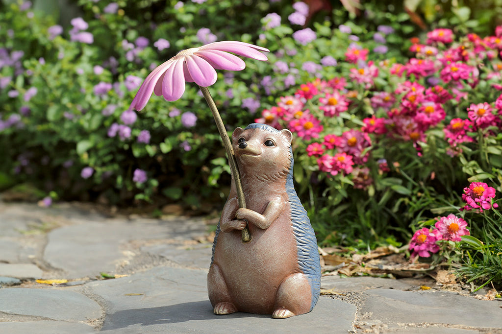 Garden sculpture of hedgehog holding flower blossom like an umbrella - shown in flower garden