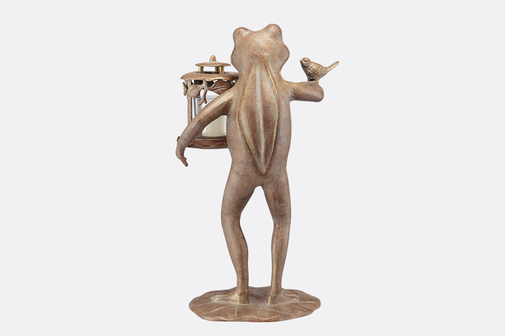 A back of a  brown statue of a frog with a bird on its arm and a lantern on its hand against a white background