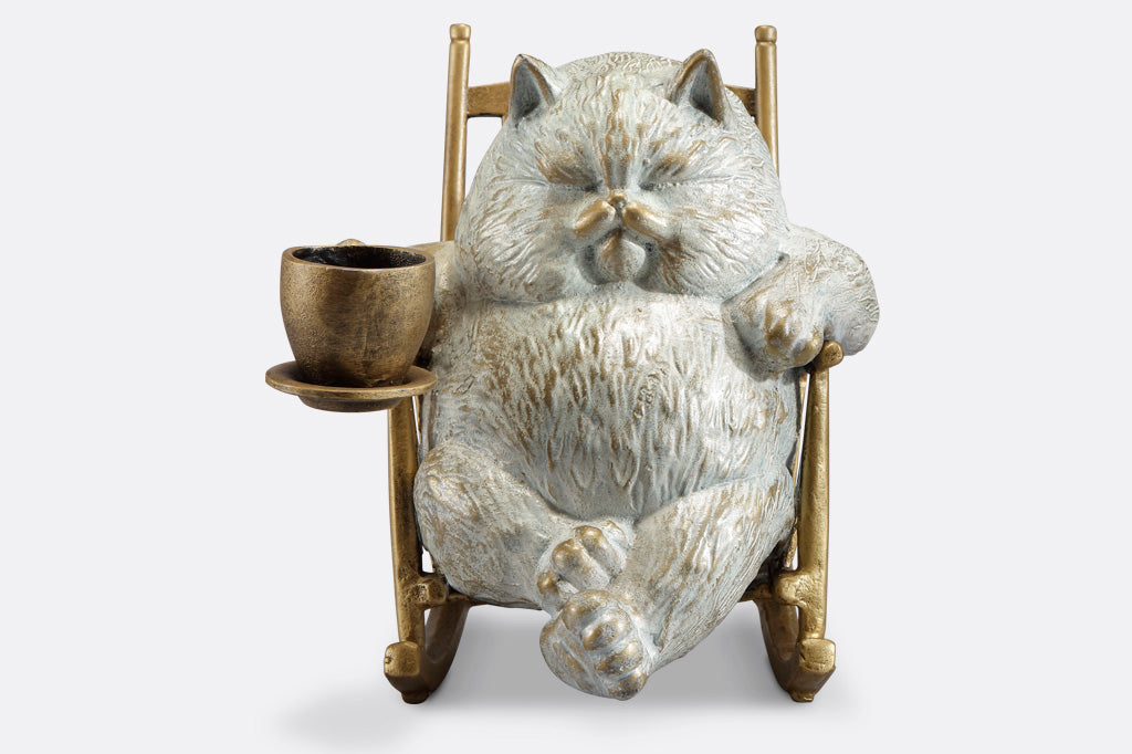 Front view of White cat in a rocking chair sculpture. Cat is restfully sitting with eye closes, holding a teacup which could hold LED tealight.