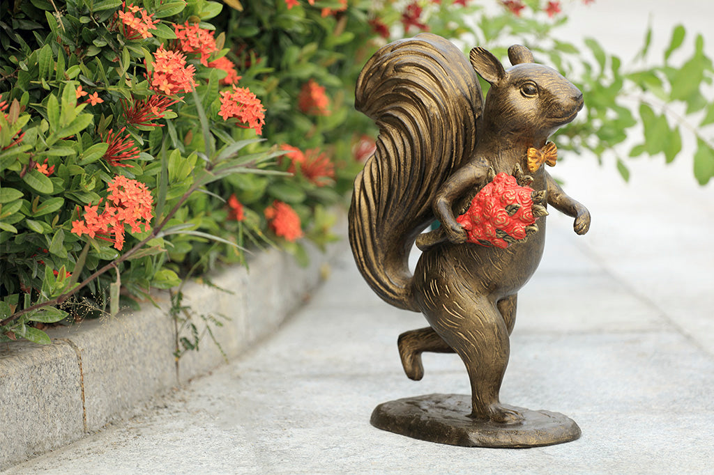 Garden sculpture of squirrel wearing bowtie, running with bouquet of red roses in its paw.