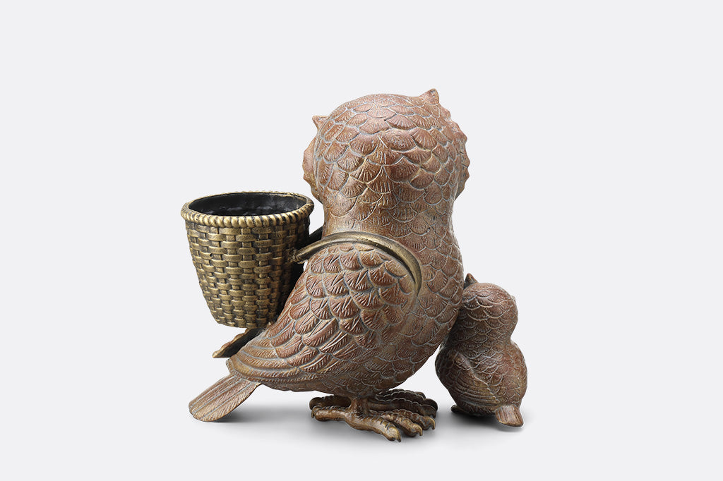 Bronze owl-shaped container with a woven basket on a white background
