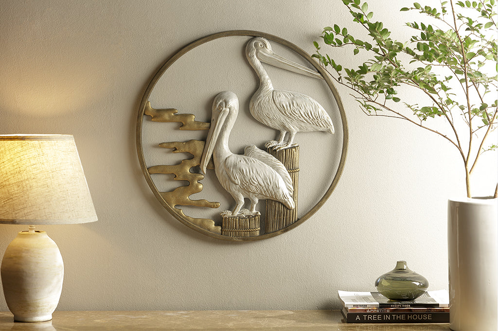 cast metal pelican wall art shown on interior wall. Staged with lamp and vase with branches 