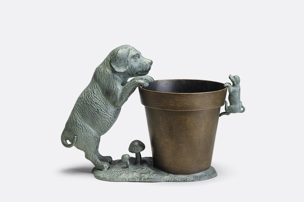 A planter statue with a small puppy holding onto the lip of the pot while a bigger dog peers over.