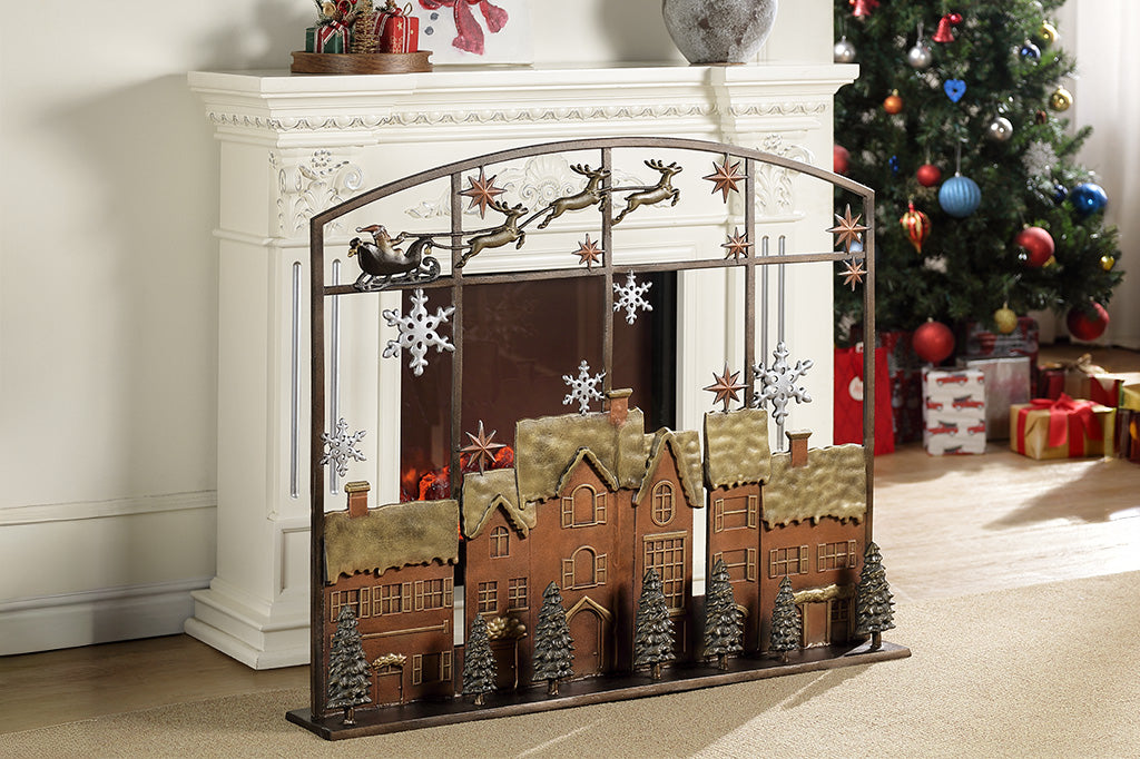 Decorative fireplace screen with village design in front of a Christmas tree and presents.