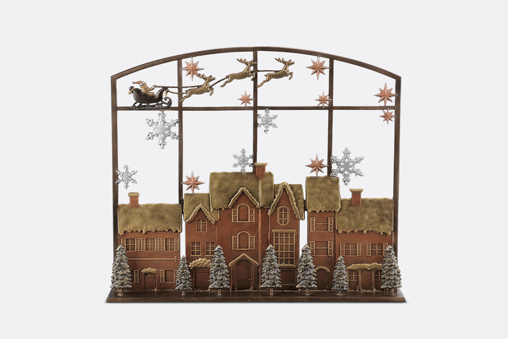 Decorative metal fireplace screen with a Christmas scene featuring Santa Claus, reindeer, and a village.