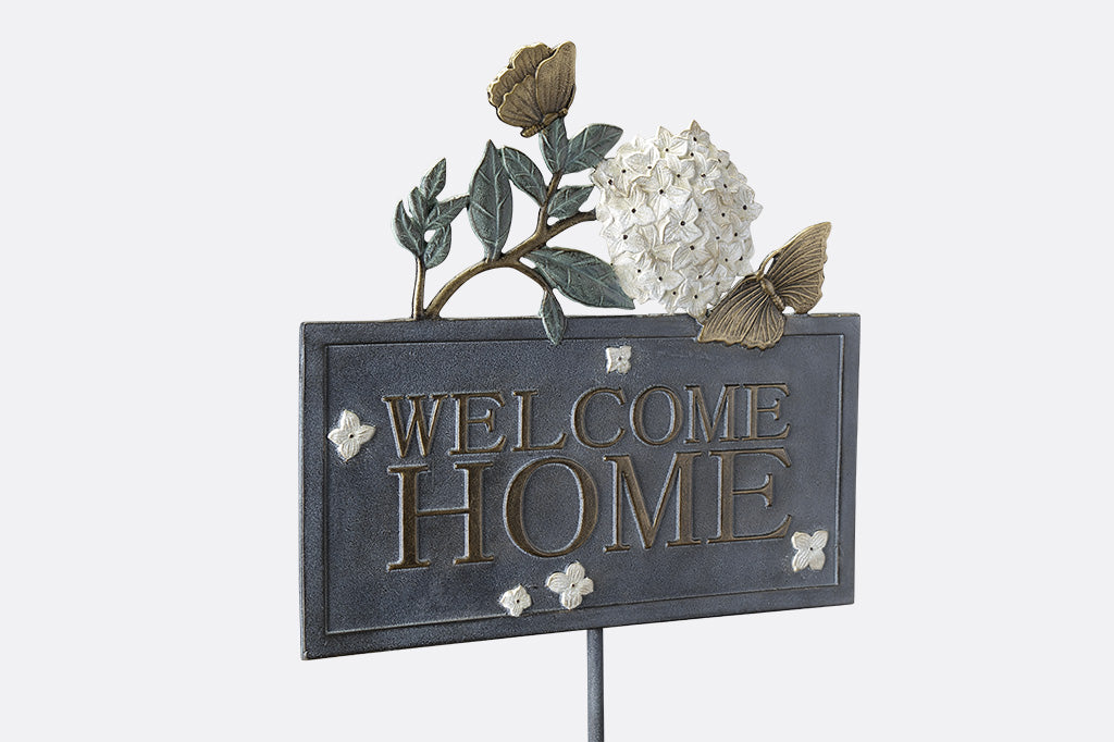 Outdoor Garden Sign with words "Welcome Home" on rectangle frame, adorned with white hydrangea blossom and golden butterflies.