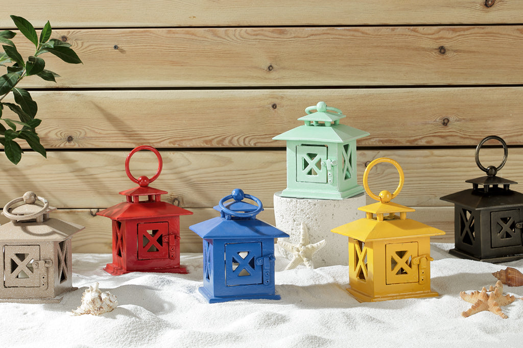 Cast metal votive candle lanterns shown on sand by seashells. 6 colors: sand, red, blue, green, yellow, bronze