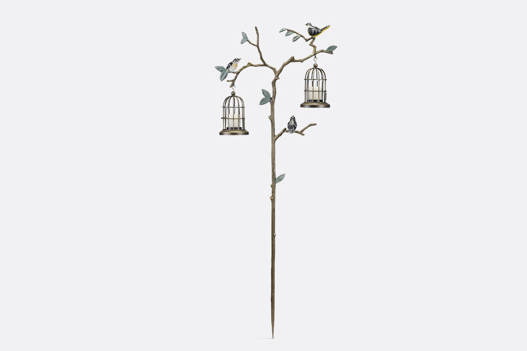 a staked garden accent with branch and leaf motif with songbirds. It supports two hanging candle lantern cages.