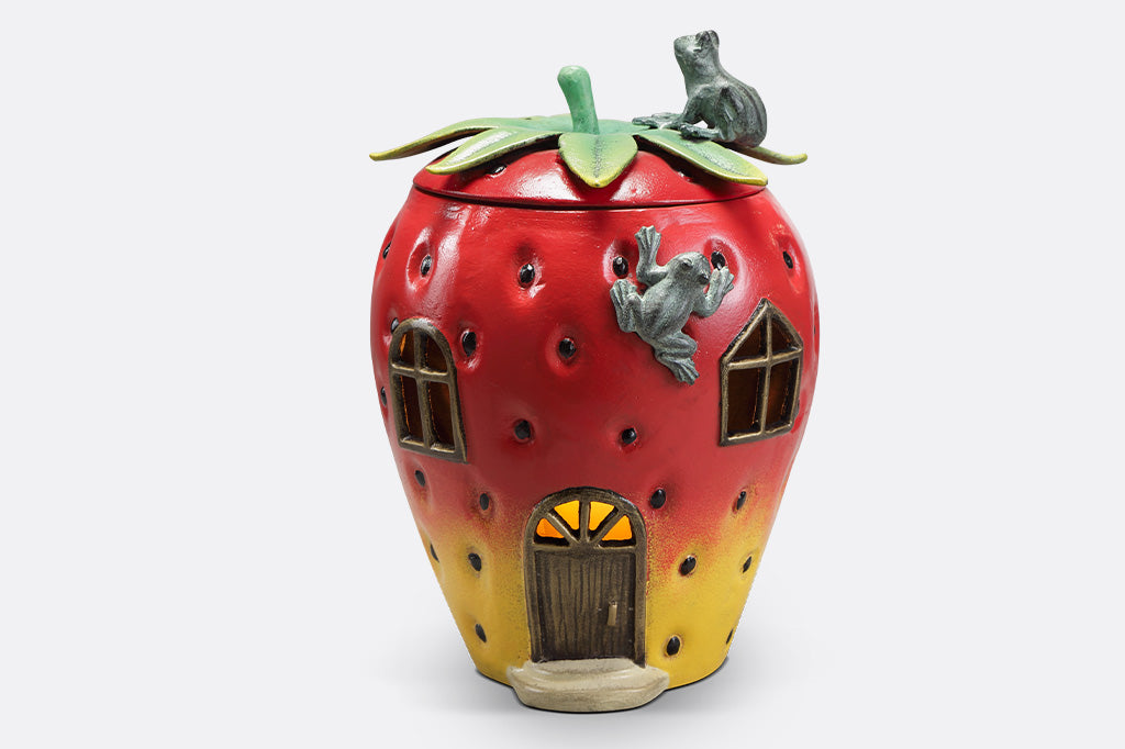 Strawberry House theme garden candle lantern with two frogs on top. Stem shaped lid comes off and candlelight shines through windows and door of strawberry house.