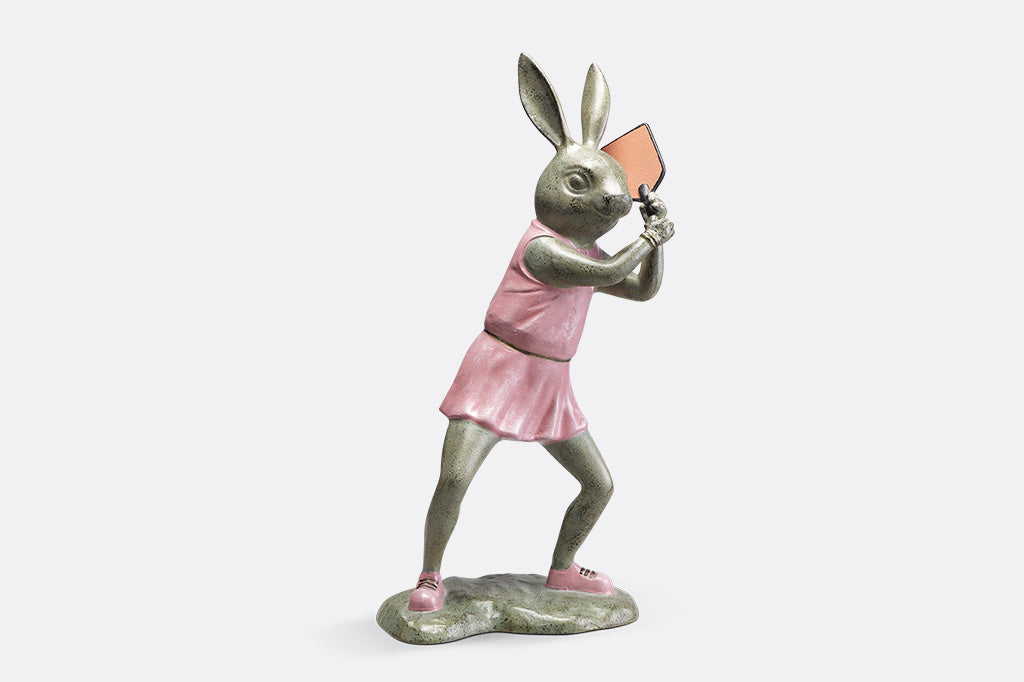 Rabbit garden sculpture with pickleball theme. She wears a pink dress, pink sneakers and holds a pink pickleball paddle 