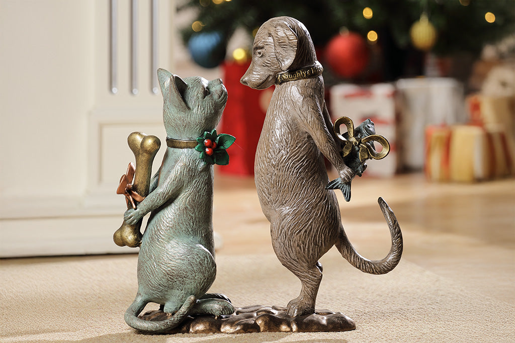 Statue of a cat holding a bone and a dog holding a fish on the floor of a living room.