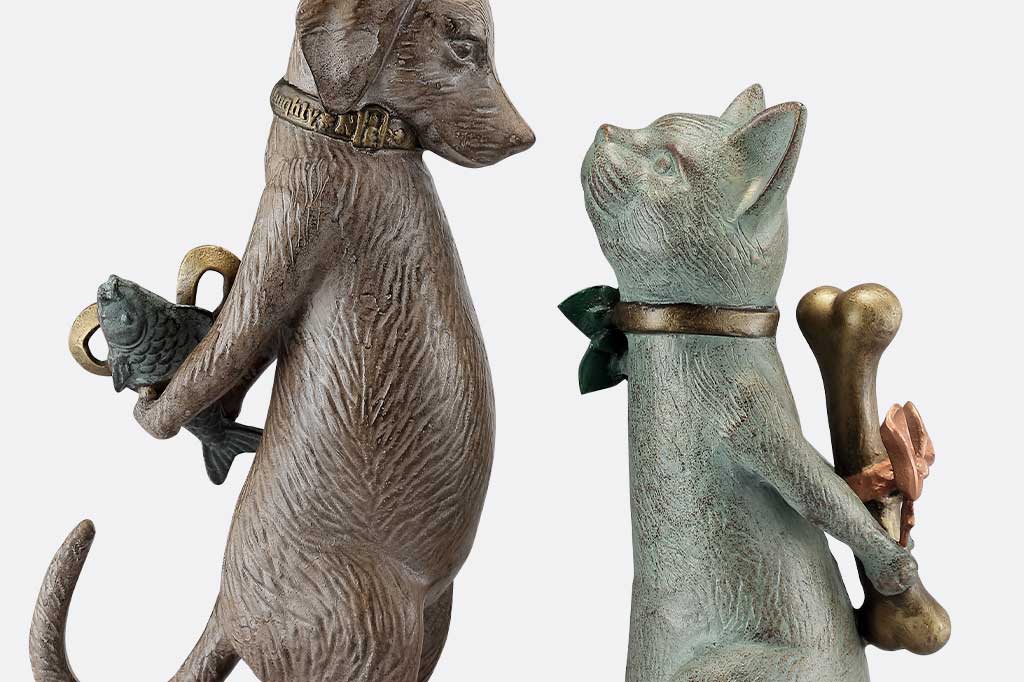 Statue of a dog and a cat holding fish and bone, respectively, on a white background.