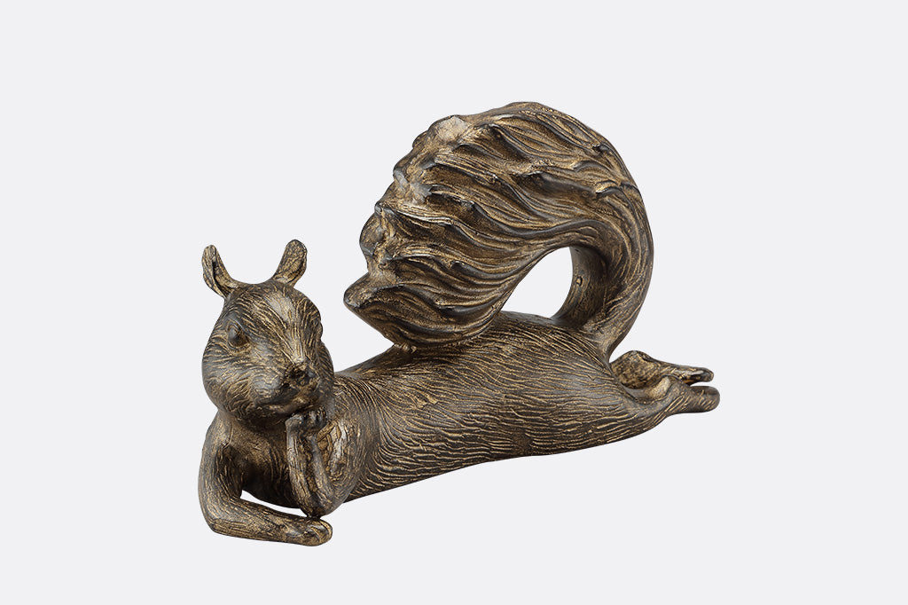 The front of a squirrel statue leaning on it's side with it's tail up, leaning it's head on it's paw.