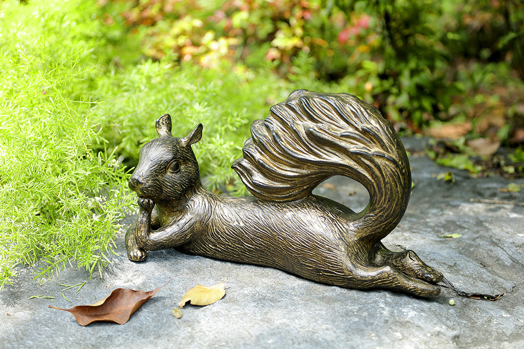 A squirrel statue leaning on it's side with it's tail up placed in a garden.