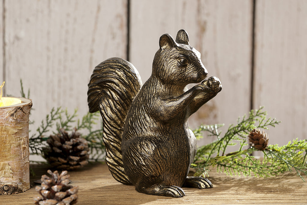 A statue of a squirrel nibbling and holding a little acorn in it's paws placed on a table with pinecones.