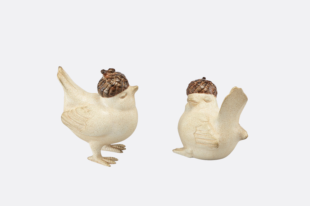 A pair of two birds, one standing, the other sitting, both wearing little acorn hats.