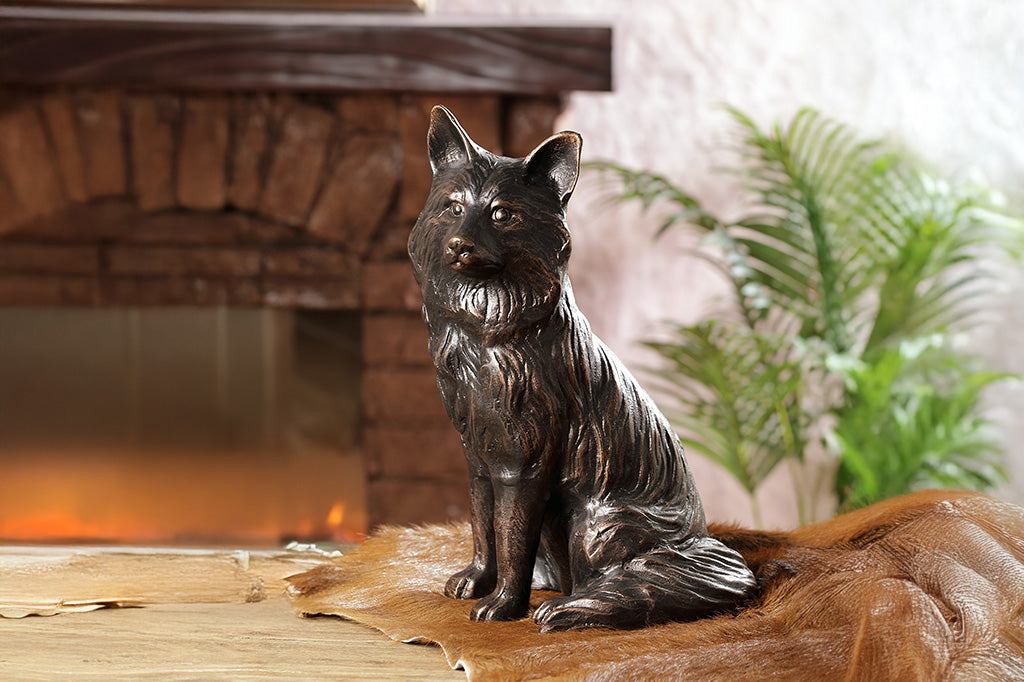 The front of a brown sculpture of a fox sitting, placed pm a fur rug in a living room.