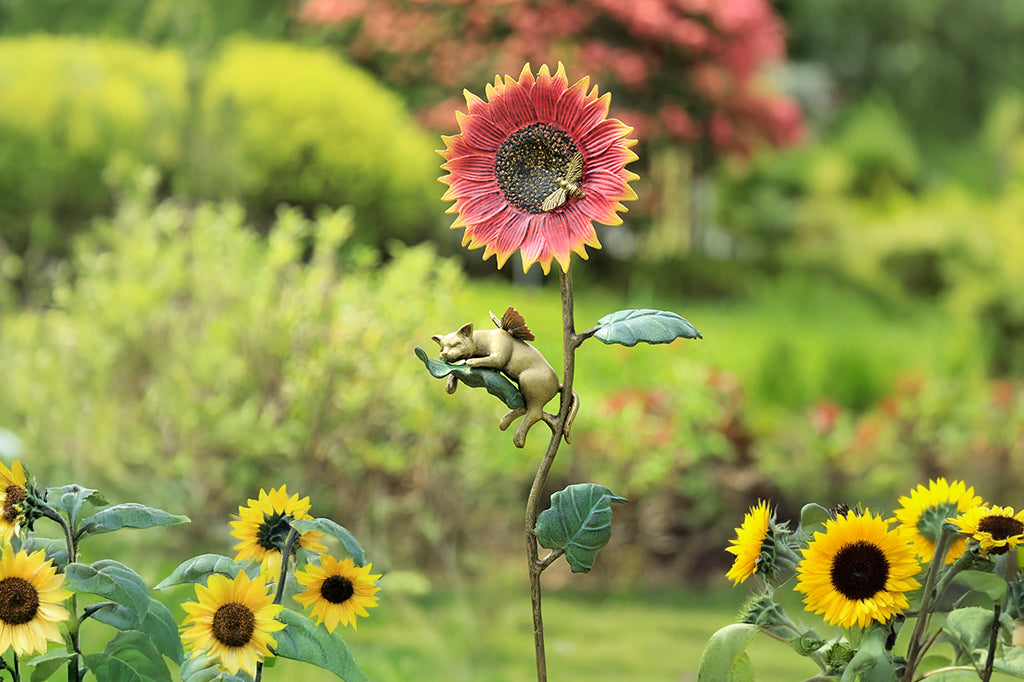 cast metal staked orange and yellow sunflower with cat napping on leaf set in garden scene 