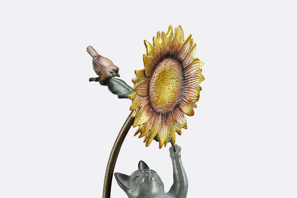 Garden stake of a cat reaching for a flower with a bird peering at it.