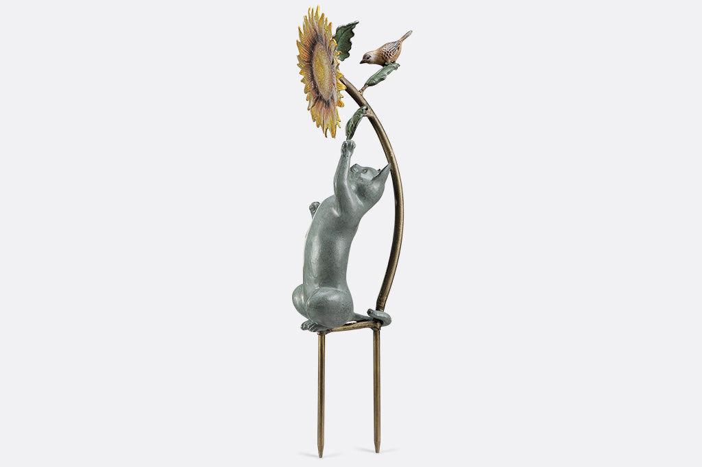 Garden stake of a cat reaching for a flower with a bird peering at it.