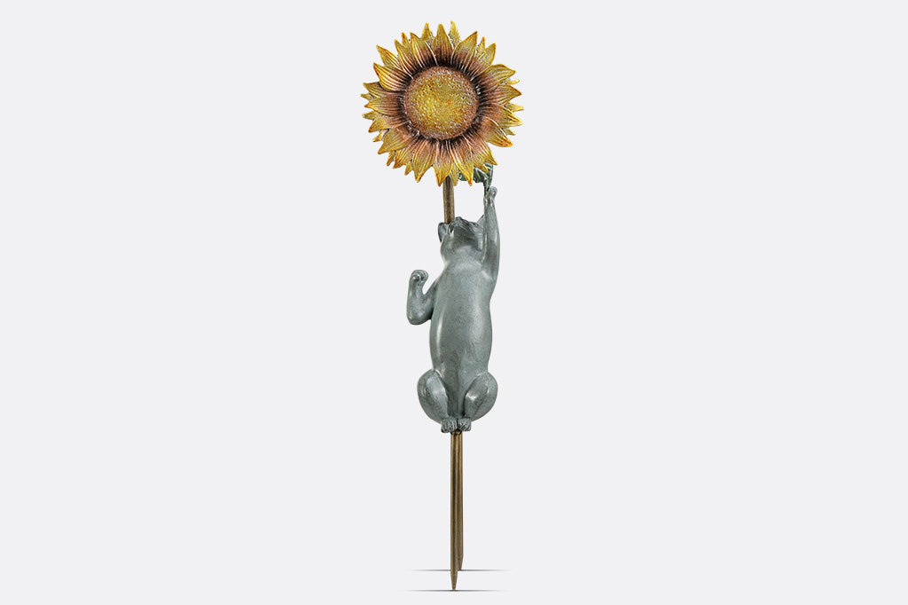 Garden stake of a cat reaching for a flower with a bird peering at it.