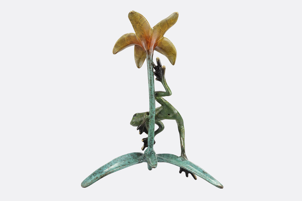 The back of a statue of a frog climbing around a yellow flower.