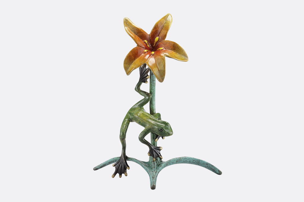 The front of a statue of a frog climbing around a yellow flower.