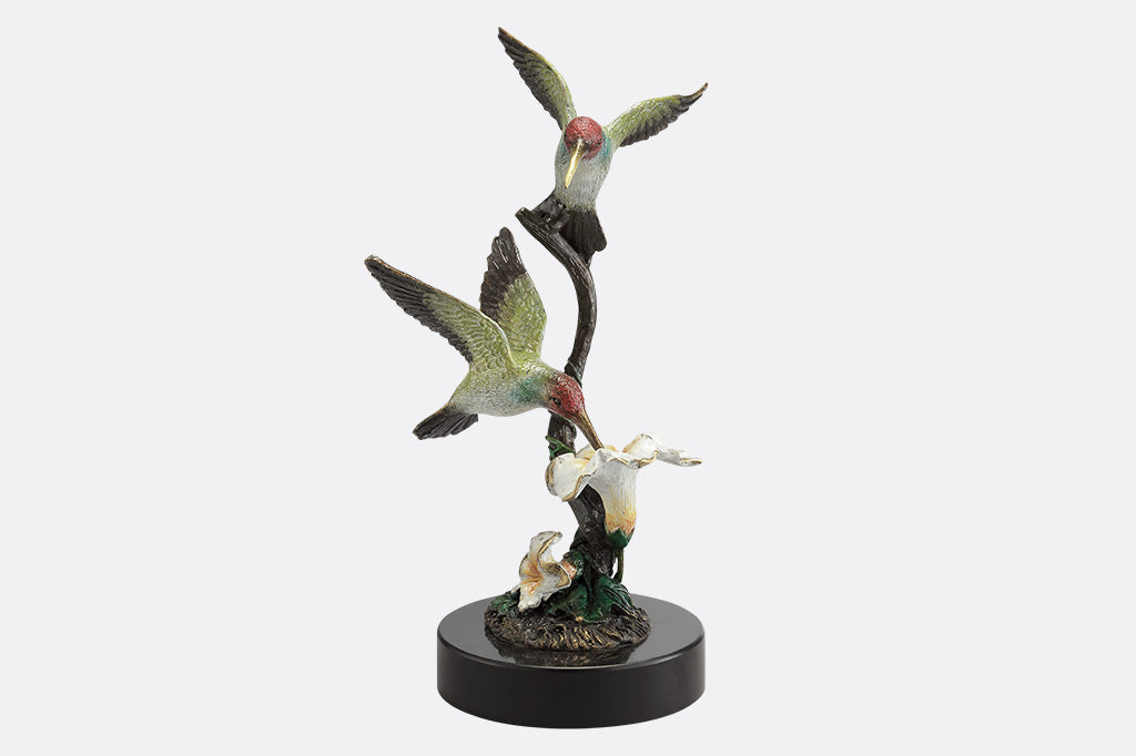 A sculpture of two birds, one perched on a branch, and another taking a sip of nectar from a flower.