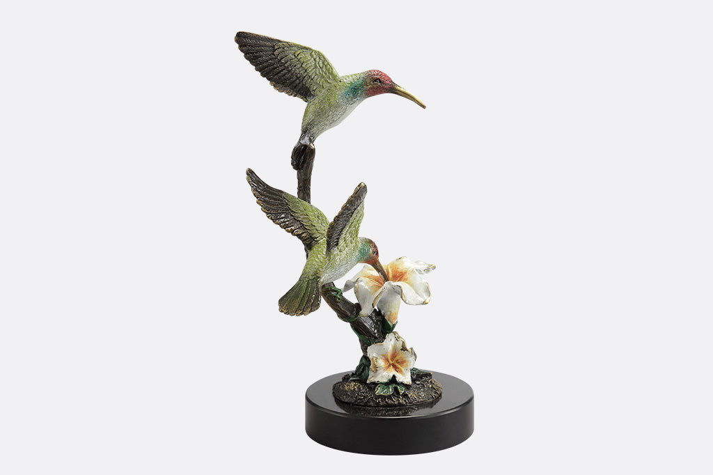 A side view of a sculpture of two birds, one perched on a branch, and another taking a sip of nectar from a flower.