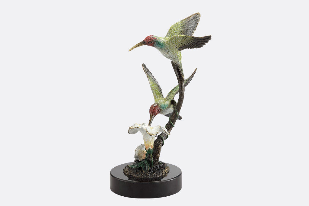 A side view of a sculpture of two birds, one perched on a branch, and another taking a sip of nectar from a flower.