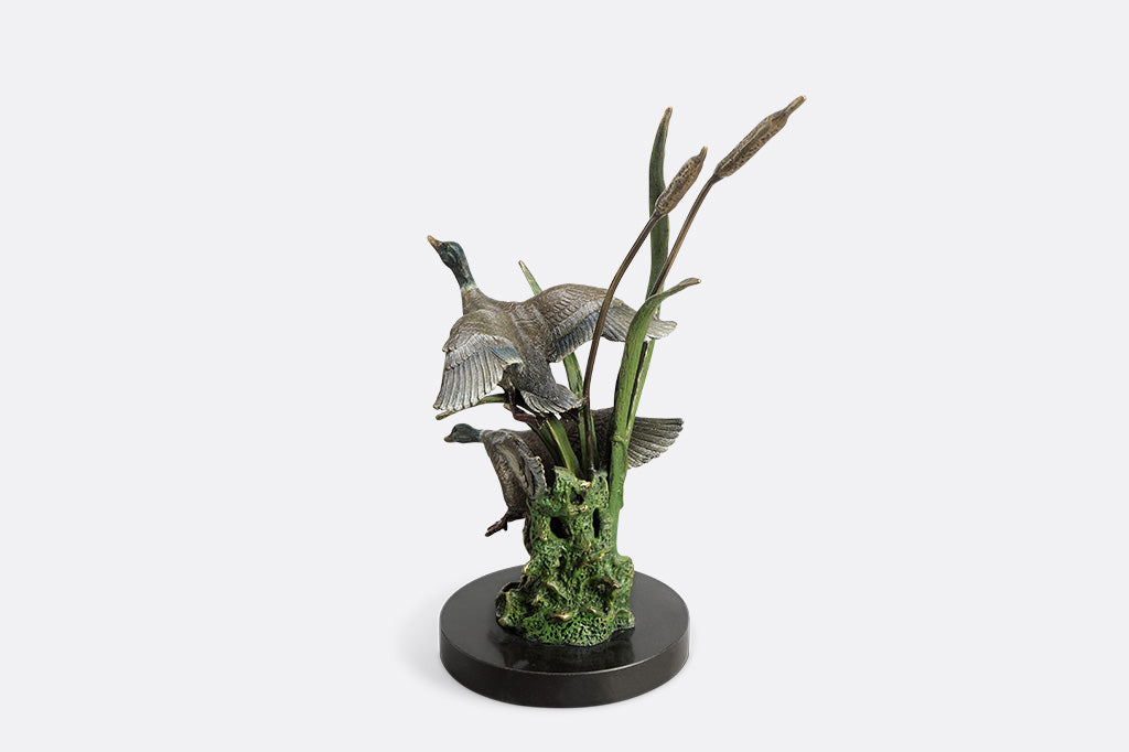 Brass sculpture of two ducks on a stand with reeds on a white background