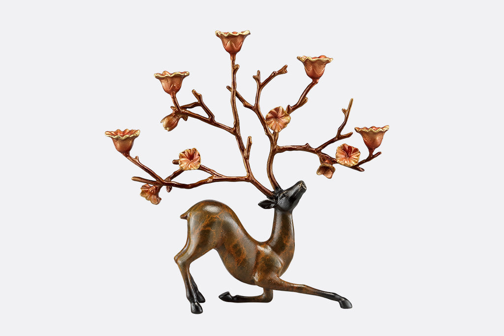 A sculpture of a kneeling stag with flowers on it's antlers which act as candle holders.