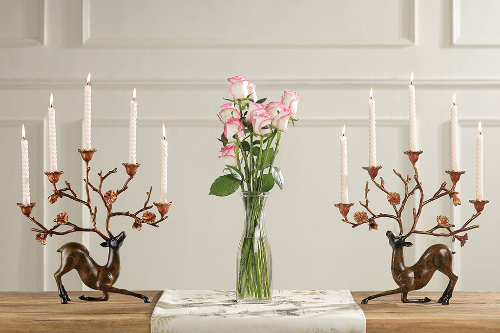 A table setting of two sculptures of a kneeling stag with flowers on it's antlers which act as candle holders.
