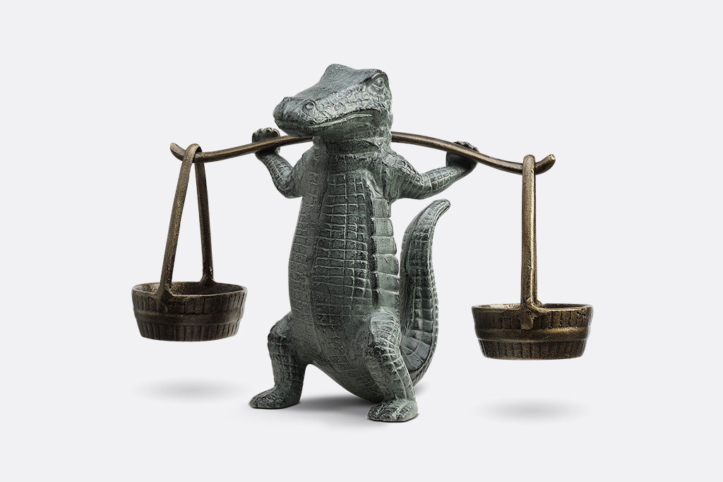 A sculpture of an alligator holding up two buckets.