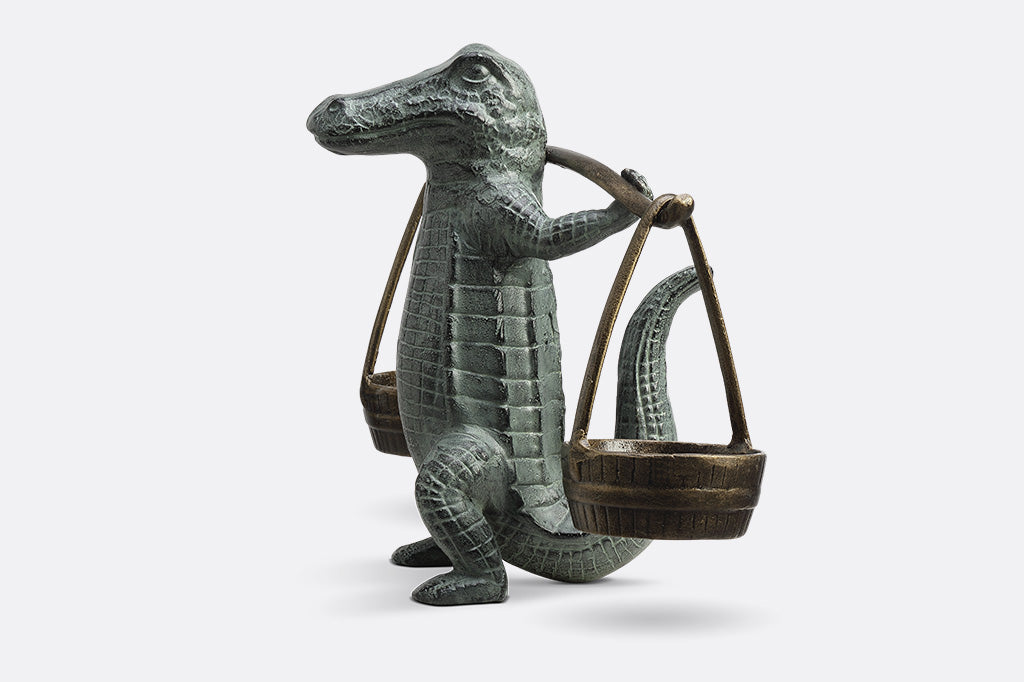 A sculpture of an alligator holding up two buckets.