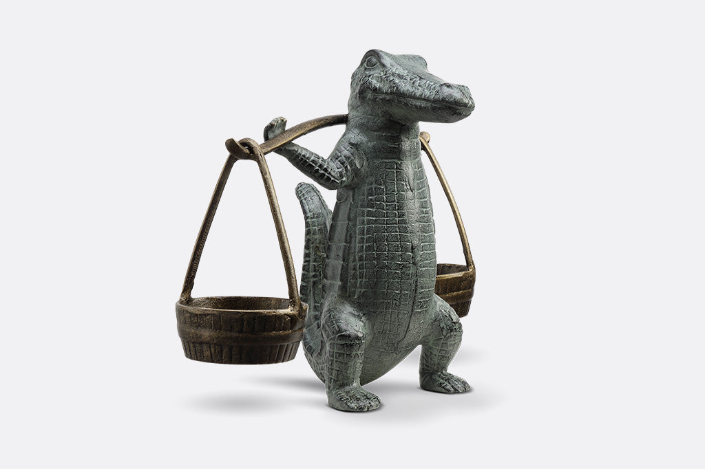 A sculpture of an alligator holding up two buckets.