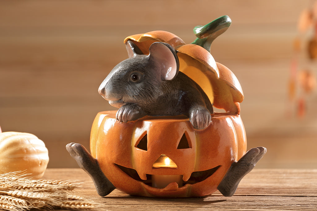 cast metal gray mouse in jack o lantern set on counter with lit votive candle 