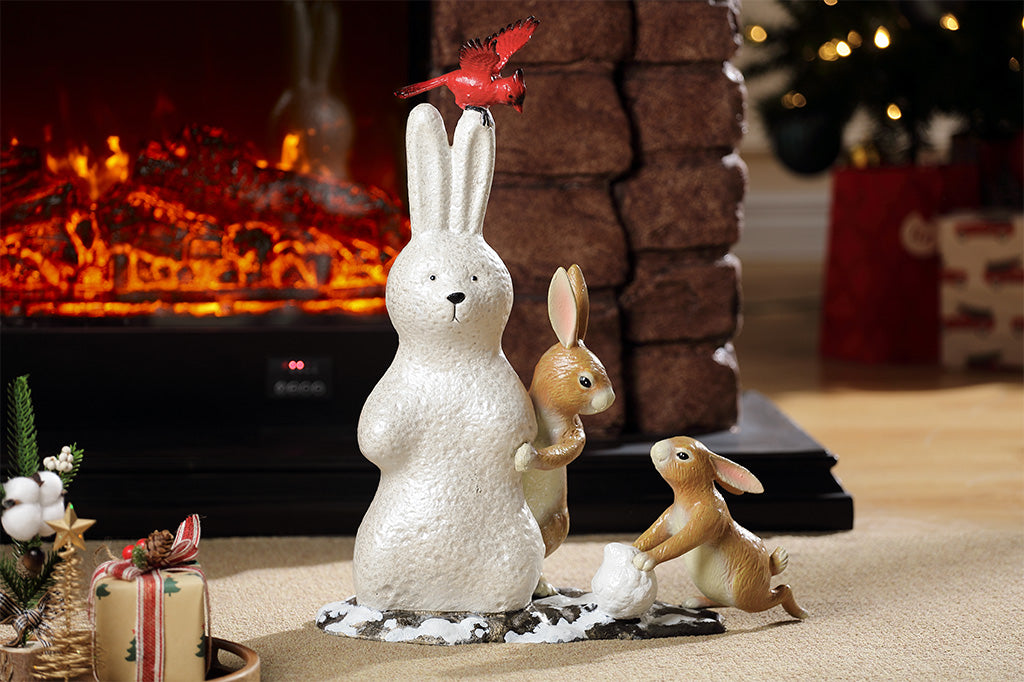 A sculpture of a pair of two bunnies building a bunny shaped snow man, while a cardinal bird hovers above placed in a living room.
