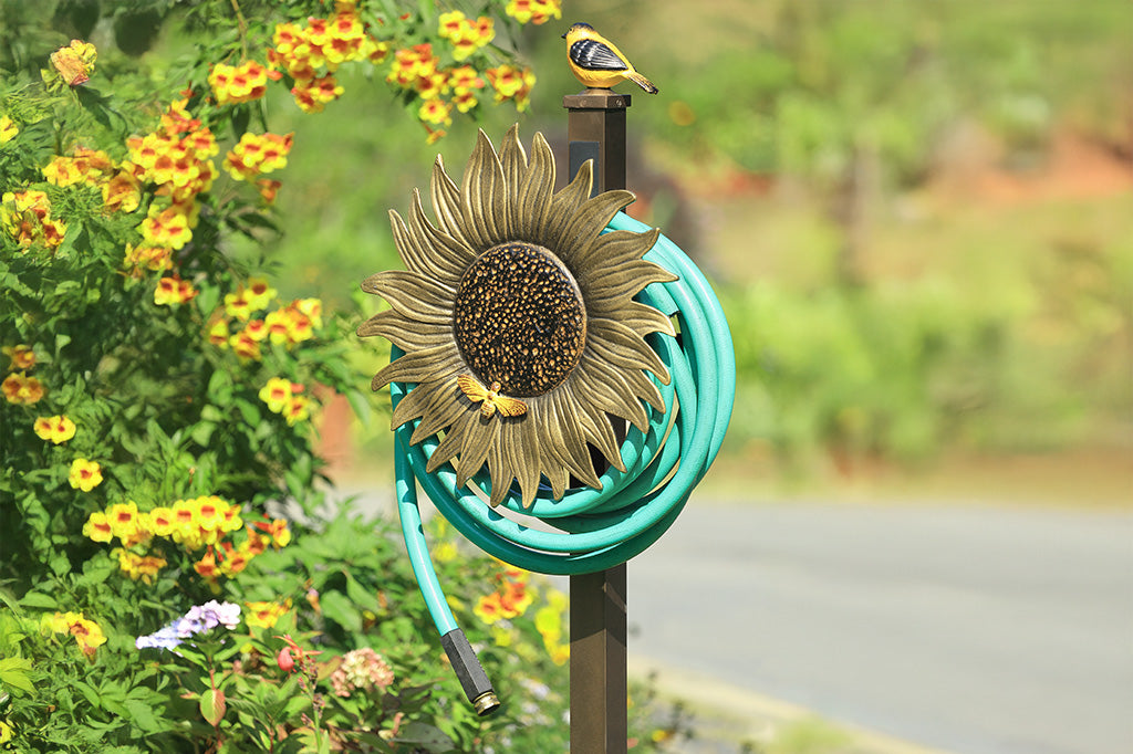 A garden stake hose holder with a sculpture of a sunflower and bird.