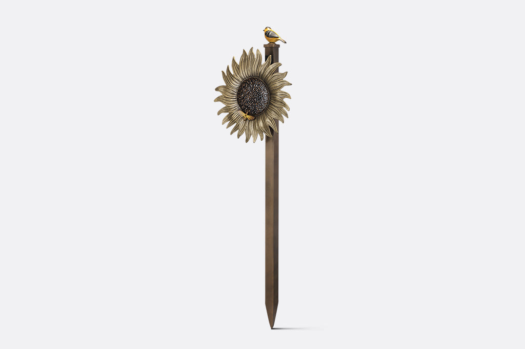 A garden stake hose holder with a sculpture of a sunflower and bird.