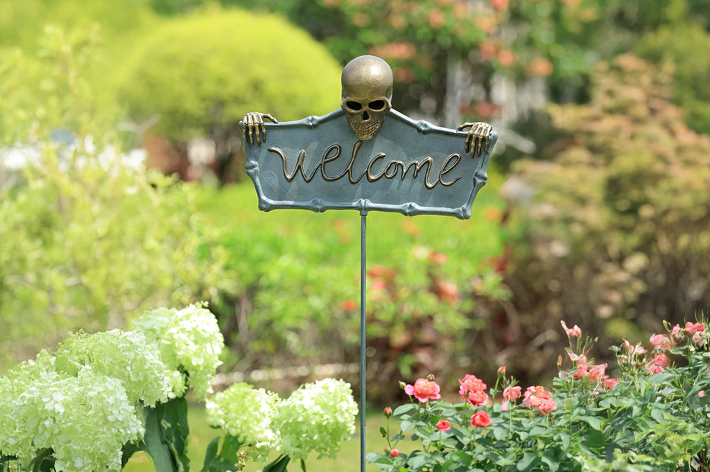 cast metal welcome sign with skeleton holding sign set in garden 