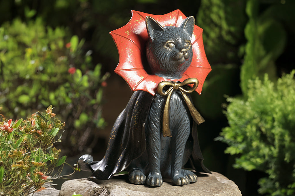 cast metal cat in cape perched on rock 
