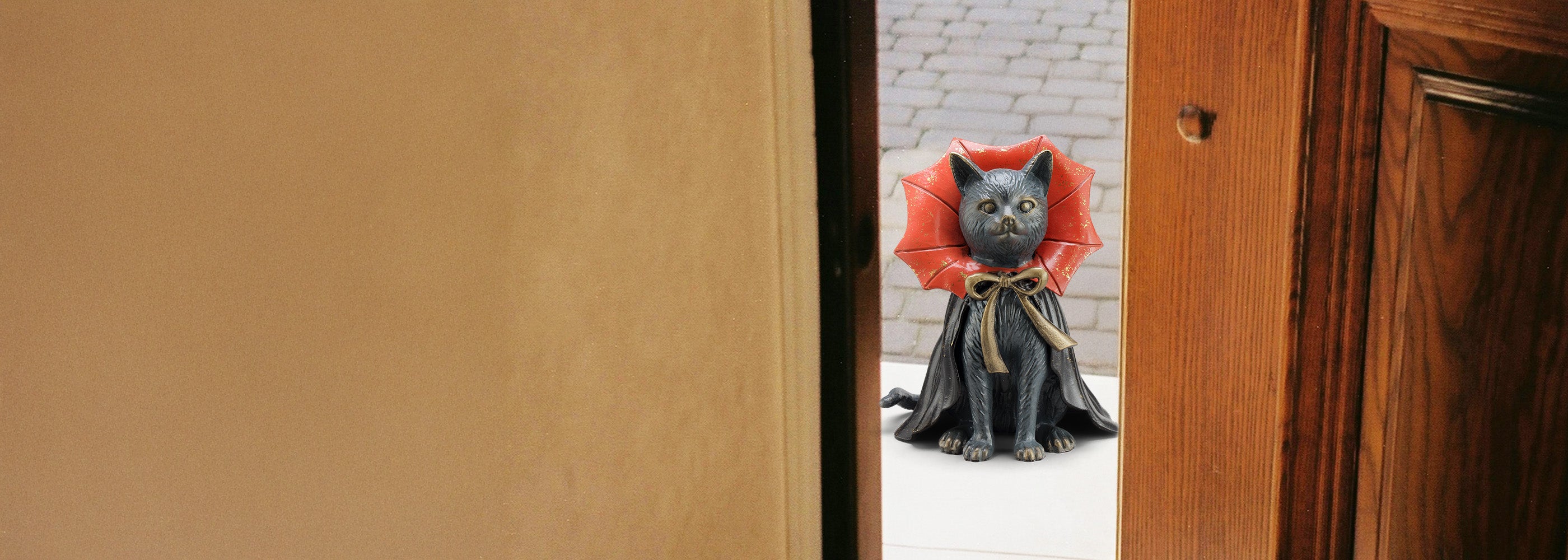 Cat wearing a red cape garden sculpture peeking from behind a wooden door as if to trick-or-treat.